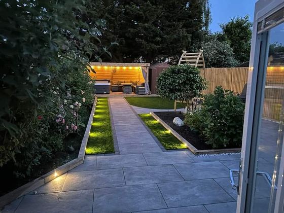 Garden at dusk with porcelain paving, artificial lawn strips, lighting and a garden room