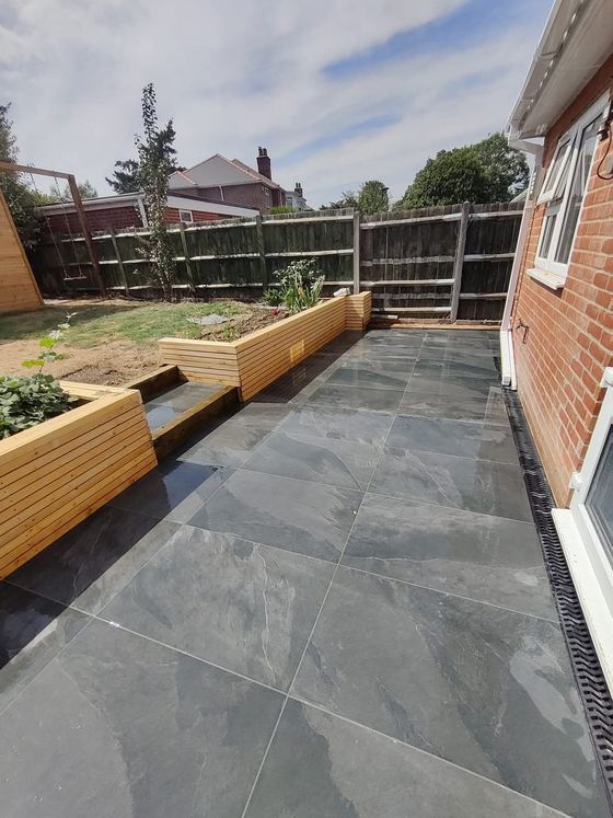 Dark porcelain patio with raised timber planters and a drainage channel