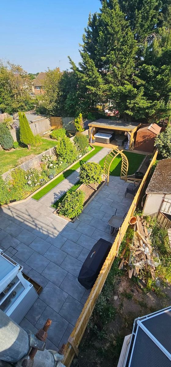Aerial view of a landscaped garden with paving, artificial lawn strips, a pergola arch and a garden room